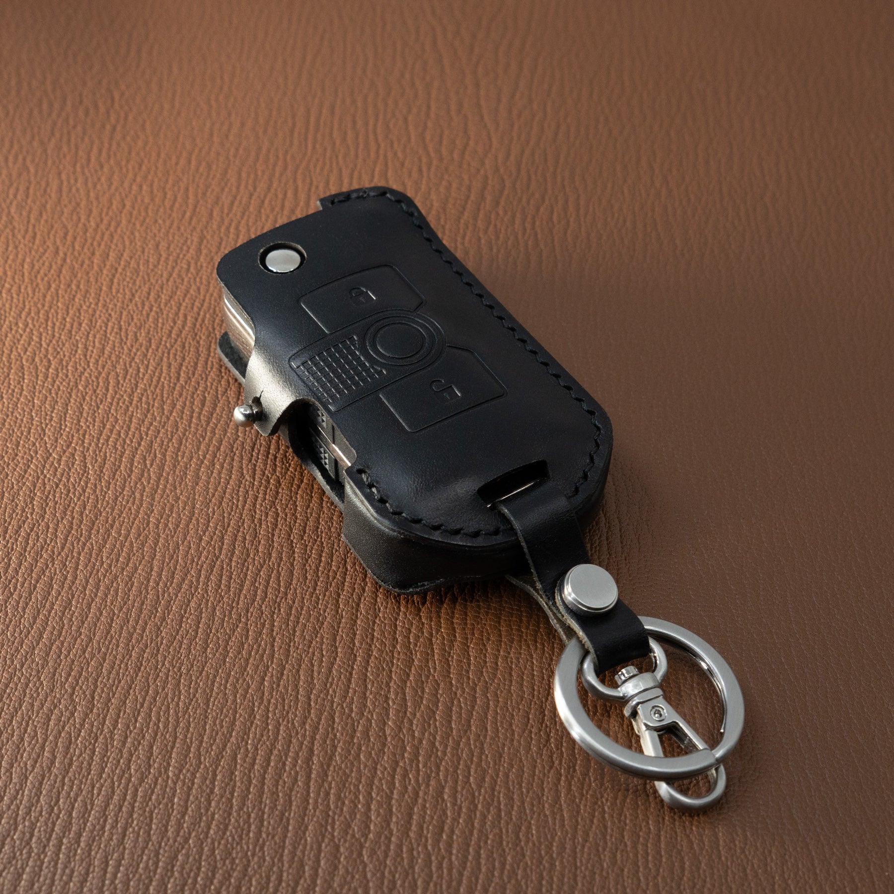 Black leather car key case with metallic clip on a brown textured background